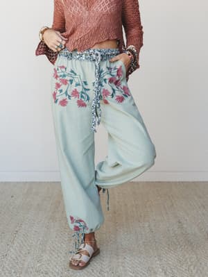 Flowy sage wide-leg pants with bold floral embroidery at the hip and ankle pair with a terracotta crochet crop top and strappy sandals — the kind of outfit that feels like a good decision the moment you put it on.