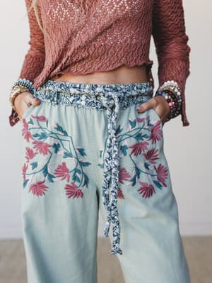 A close-up of sage wide-leg pants with bold floral embroidery paired with a dusty rose open-knit top — the kind of outfit that feels like it was put together effortlessly but definitely wasn't.