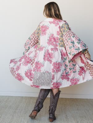 Shot from behind, a model twirls in a voluminous patchwork floral jacket paired with dark brown cowboy boots — the kind of piece that looks like it was made from the prettiest quilt you've ever seen.