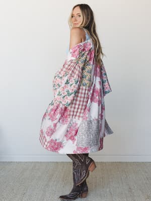 A model shot in profile wearing a voluminous floral patchwork duster jacket over a light blue top, paired with dark brown cowboy boots — the kind of piece that looks like it was stitched together from someone's most-loved vintage fabrics.