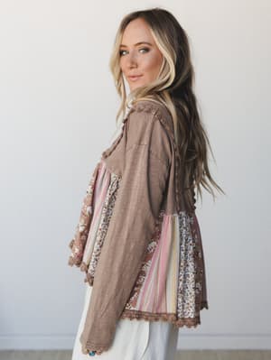 A model shot from a three-quarter back angle showing a relaxed boho patchwork top in tan with mixed floral and stripe panels — the kind of top that looks like it has a whole story behind it.