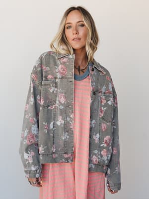 An oversized floral-printed denim jacket in washed khaki layered over a coral striped dress — the kind of outfit that looks like it came together effortlessly but you know she thought about it.