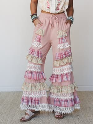 A dreamy pair of wide-leg pink pants covered in alternating tiers of floral, plaid, and lace ruffles — styled with an embroidered crop top, stacked bracelets, and sandals for a look that has absolutely committed to the bit in the best way.