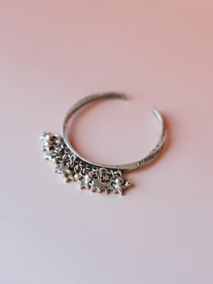 A pewter-toned cuff bracelet with dangling star charms and tiny ball accents, shot against a soft blush background with a shallow depth of field that gives it a dreamy, personal feel.