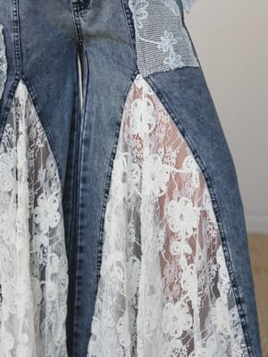 A close-up detail shot of wide-leg denim jeans with dramatic lace panel inserts — the kind of piece that can't decide between a rodeo and a wedding, and is better for it.