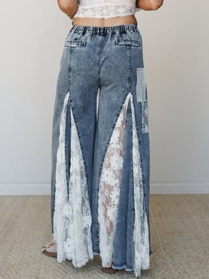 A back-view shot of wide-leg acid wash jeans with dramatic lace panel inserts running from mid-thigh to the hem, paired with a cropped lace top — the kind of outfit that makes you feel like you invented your own category.