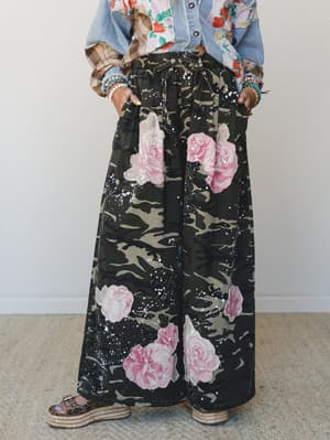 Wide-leg pants in a camo-and-rose mashup print styled with a denim jacket and stacked bracelets — the kind of outfit that looks like it shouldn't work but absolutely does.