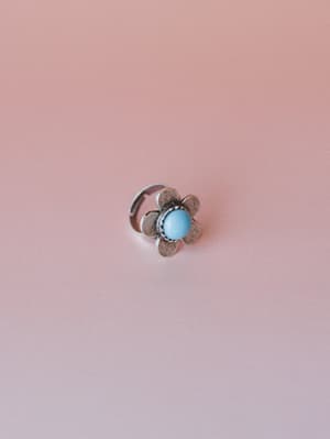A dainty silver flower ring with a sky blue stone center, shot clean against a blush pink backdrop — the kind of little thing that makes an outfit feel intentional.