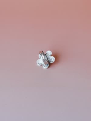 A small flower-shaped marble-effect ring sits centered against a soft dusty rose backdrop — the kind of little detail that pulls a whole look together.