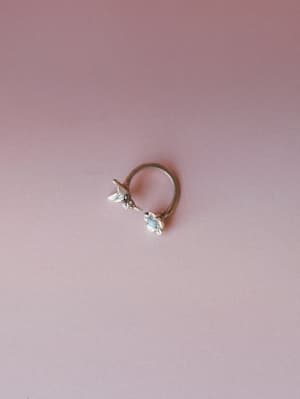 A delicate silver ring with a turquoise stone and bird charm detail, shot against a soft dusty rose background — the kind of piece you'd wear every day and never take off.