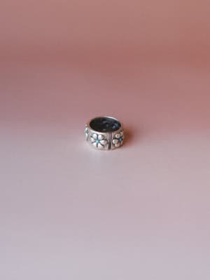 A chunky silver band ring with embossed floral panels and tiny turquoise center stones, shot solo against a warm dusty rose gradient — the kind of piece you reach for every single day without thinking about it.