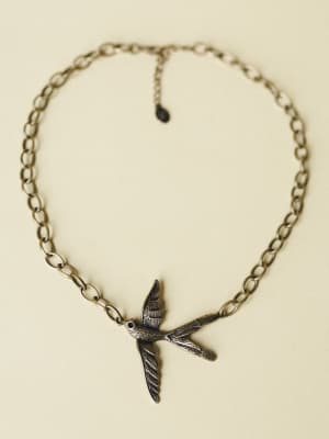 A chunky bronze chain necklace laid flat, centered by a detailed oxidized bird pendant mid-flight — the kind of piece that feels like it has a story before you even put it on.