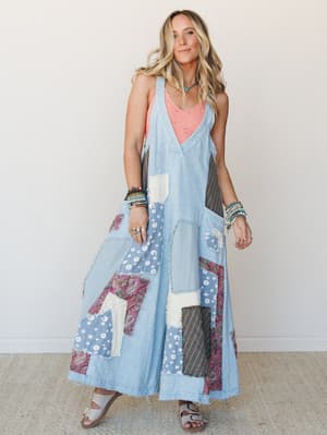 A patchwork maxi overall dress in washed denim layered over a coral tank, styled with stacked beaded bracelets and sandals — free-spirited and effortlessly collected.