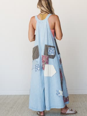 Shot from the back, this wide-leg denim jumpsuit is covered in mismatched patchwork appliqués — florals, paisleys, stripes — giving it the energy of a well-loved quilt that decided to become an outfit.