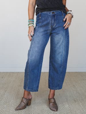A mid-shot of wide-leg barrel jeans in medium denim wash, styled with a dark tee, leopard print mules, and a stack of beaded bracelets — the kind of effortless, put-together look that works just as hard at brunch as it does running errands.