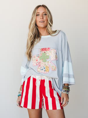 An oversized light blue top with a patchwork floral appliqué paired with bold red and cream vertical stripe shorts — the kind of mix-and-match outfit that looks like it happened effortlessly but absolutely did not.