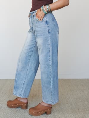 A side-angle shot of light wash wide-leg jeans styled with brown clogs and a stack of turquoise bracelets — the kind of effortless, lived-in denim that makes you want to grab coffee and wander somewhere.