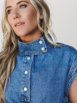A close-up model shot of a medium-wash denim vest with a structured mock neck and silver snap buttons — the kind of piece that pulls a whole outfit together without trying too hard.