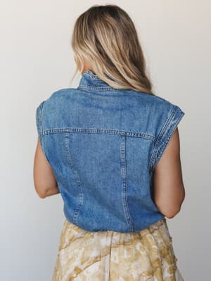 A back-view shot of a cropped denim vest styled over a tie-dye midi skirt in warm golden tones — casual and effortlessly layerable, the kind of outfit that works just as hard at brunch as it does wandering a weekend market.