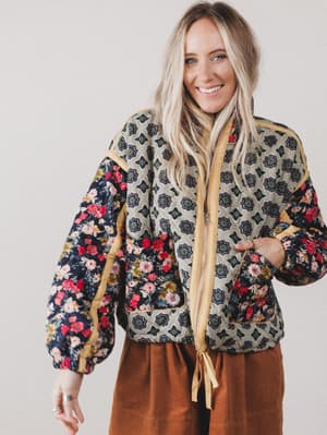 Woman wearing a patterned jacket with floral and geometric designs on a plain background