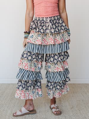 A statement-making pair of tiered ruffle wide-leg pants in mixed navy, coral, and cream prints styled with a coral textured crop top, stacked bead bracelets, and white sandals — playful, expressive, and completely unapologetic.