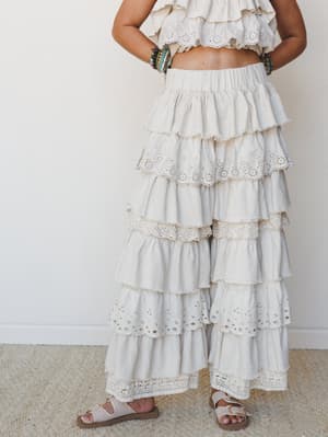 A tiered, ruffle-heavy wide-leg pant in soft cream-taupe paired with a matching eyelet crop top — the kind of outfit that makes every walk feel like a slow-motion moment in a sun-drenched courtyard.