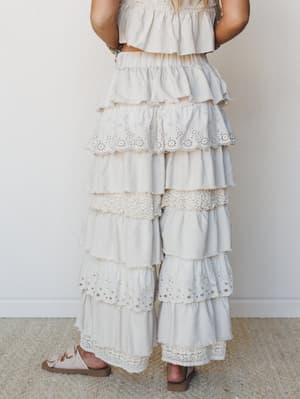 A dreamy head-to-toe cream set shot from the waist down — the star is a pair of wide-leg tiered ruffle pants with alternating eyelet and lace trim details that feel like something borrowed from a romanticized past.