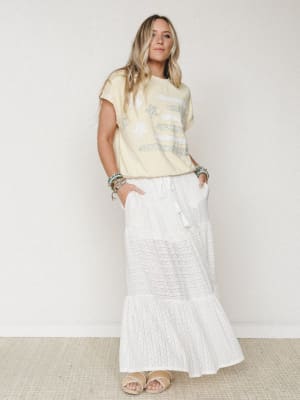 A relaxed, sun-warmed outfit pairing a butter yellow graphic tee with a flowy white maxi skirt — the kind of look that feels effortless on a Saturday with nowhere urgent to be.