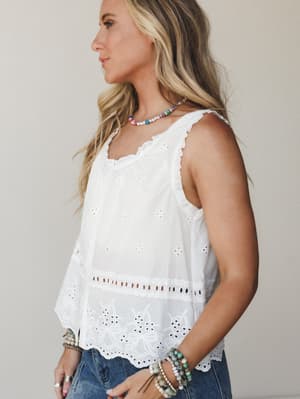 A white eyelet tank top styled with denim and layered beaded bracelets — the kind of top that feels like summer without trying too hard.