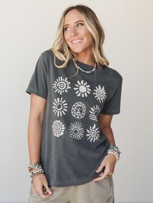 A washed charcoal graphic tee printed with nine sun motifs in a vintage stamp style, styled with layered beaded bracelets and a colorful seed bead necklace — the kind of shirt that makes a Saturday feel intentional.