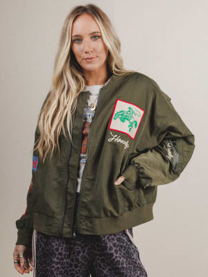 Woman wearing a green bomber jacket with patches on a plain background