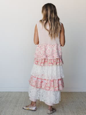 Shot from behind, a model in a dreamy tiered maxi duster layers waffle-knit texture over cascading lace and mixed floral-print ruffles — the kind of piece that looks like it was made from vintage fabrics someone loved too much to cut up.