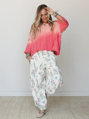 A relaxed, color-saturated outfit pairing an oversized coral ombre cable-knit sweater with wide-leg floral pants — the kind of look that feels effortless but clearly thought through.