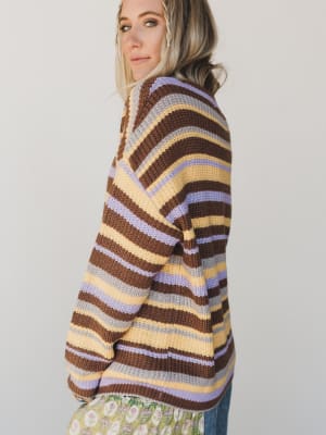 Person wearing a striped sweater with brown, purple, and yellow colors on a plain background