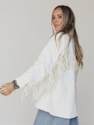 Woman wearing a white fringe jacket against a plain background