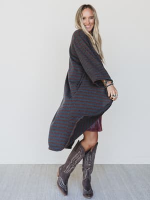 Woman wearing a long, dark-colored striped coat, standing against a white wall.