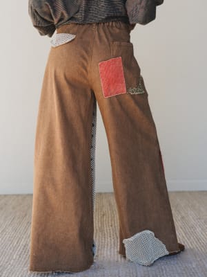 Brown corduroy pants with red pocket and silver accents on a plain background