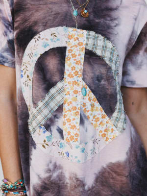 Floral peace sign design on a tie-dye shirt with visible tattoos.