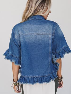 A woman with long blonde hair is shown from the back, wearing the Scottie Ruffle Denim Jacket - Blue, featuring a cropped hemline and ruffled trim on the sleeves and hem. She accessorizes with several bracelets on her right wrist.