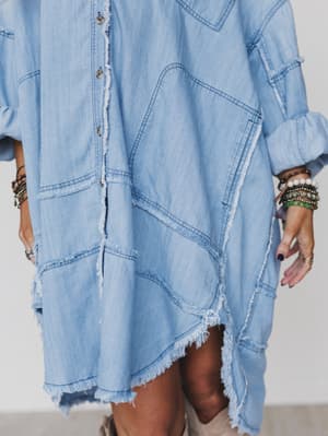 Wearing the Ophelia Oversized Denim Dress in washed denim, this person pairs its frayed edges and patchwork details with rolled-up sleeves and beaded bracelets for a relaxed, boho-inspired look.