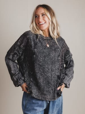 Woman wearing a black acid-wash sweater and blue jeans against a plain background