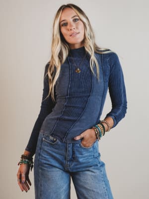 Woman wearing a blue denim jacket over a black long-sleeve shirt with jeans, standing against a plain background.