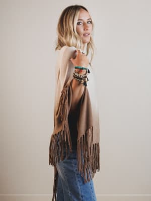 Woman wearing a beige fringe poncho with a plain background