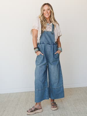 Wide-leg denim overalls styled with a blush lace top, stacked beaded bracelets, and platform sandals — the kind of effortless, lived-in outfit that feels equally at home at a farmers market or a summer music festival.