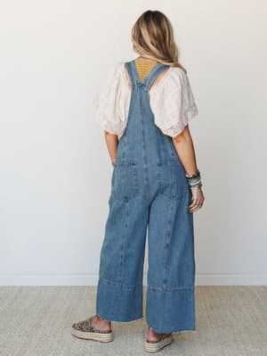 Shot from the back, this look pairs wide-leg denim overalls with a blush lace-trim top and stacked boho bracelets — the kind of outfit that makes a farmers market run feel like a whole personality.