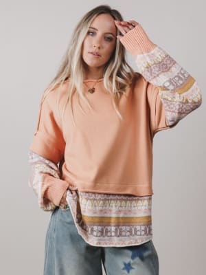 Woman wearing a peach-colored sweatshirt with patterned sleeves against a plain background