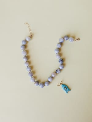 A grey marbled stone bead necklace laid flat with a detached turquoise fish charm pendant beside it — earthy, collected, and quietly coastal.