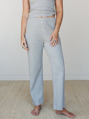 Heather grey ribbed wide-leg pants styled as a matching set with a coordinating tank, shot from the waist down with a soft, lived-in interior feel — the kind of outfit that makes staying home look intentional.