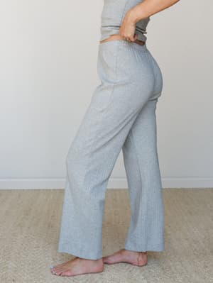 A side-profile shot of wide-leg ribbed knit pants in heather grey, styled with a matching grey top and worn barefoot — soft, relaxed, and the kind of outfit you'd genuinely hate to change out of.