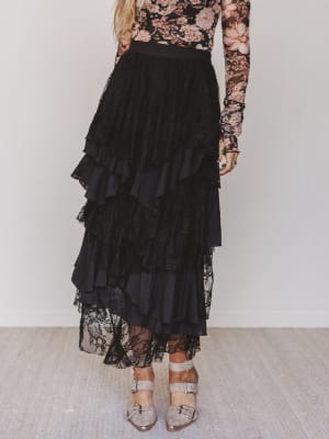 Person wearing a black ruffled skirt with a floral top against a white background